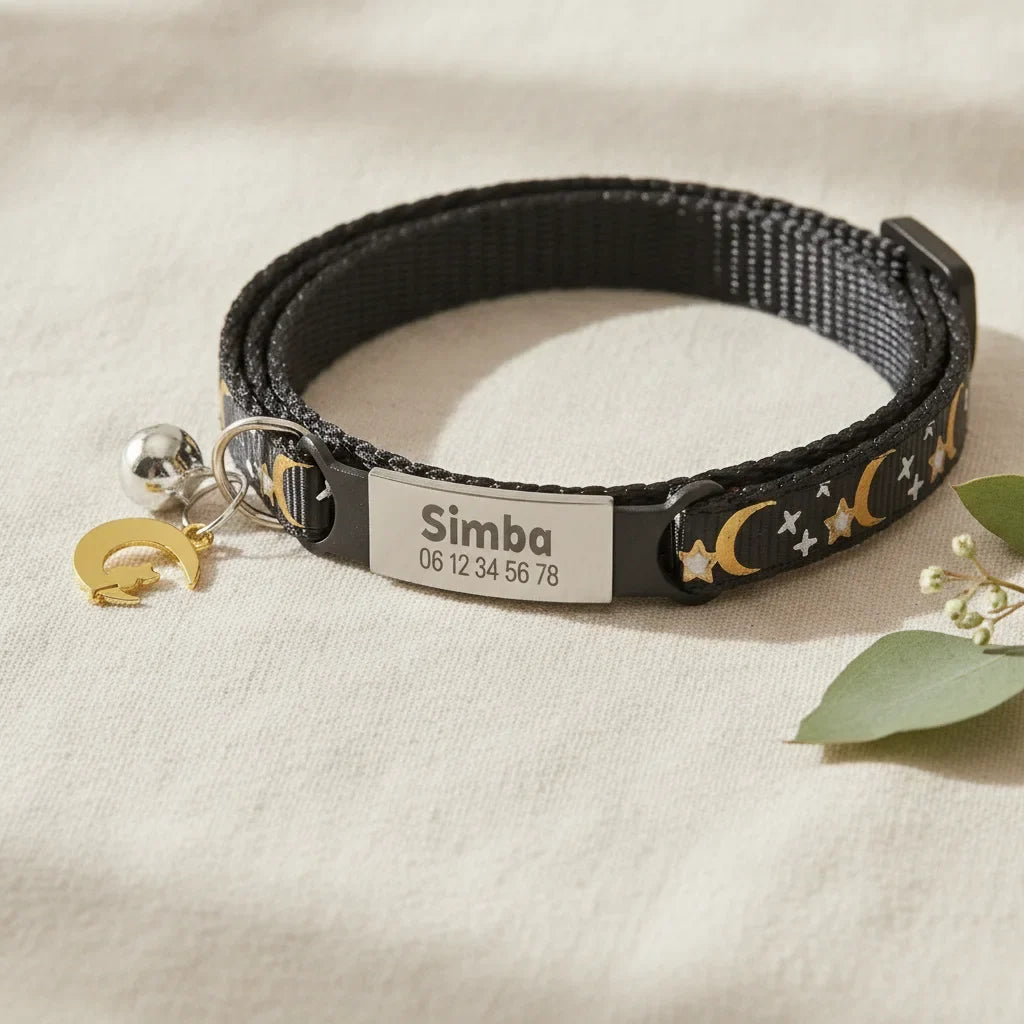 Gros plan sur la plaque gravee personnalisee (nom et numero) d'un collier pour chat noir a motif lune et etoiles
